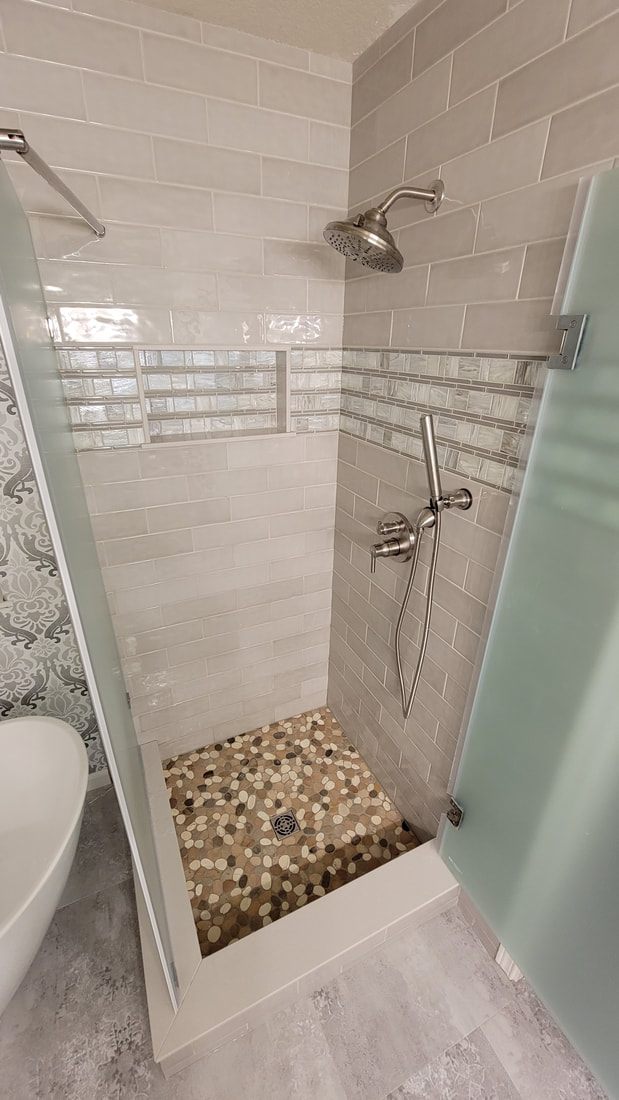 Finished custom tiled shower with a pebble floor and frameless glass enclosure