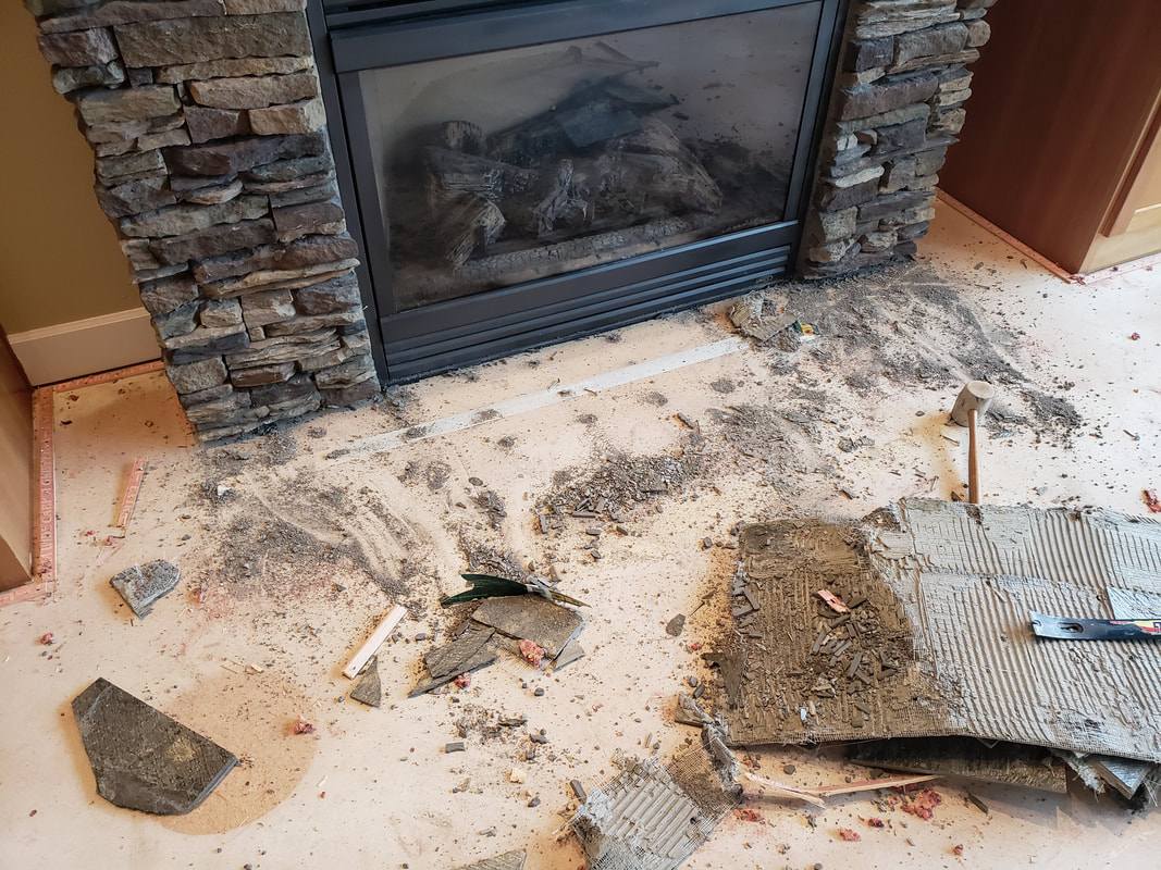 The same fireplace with the old hearth demolished — broken tile, thinset and backer mesh lifted off the floor