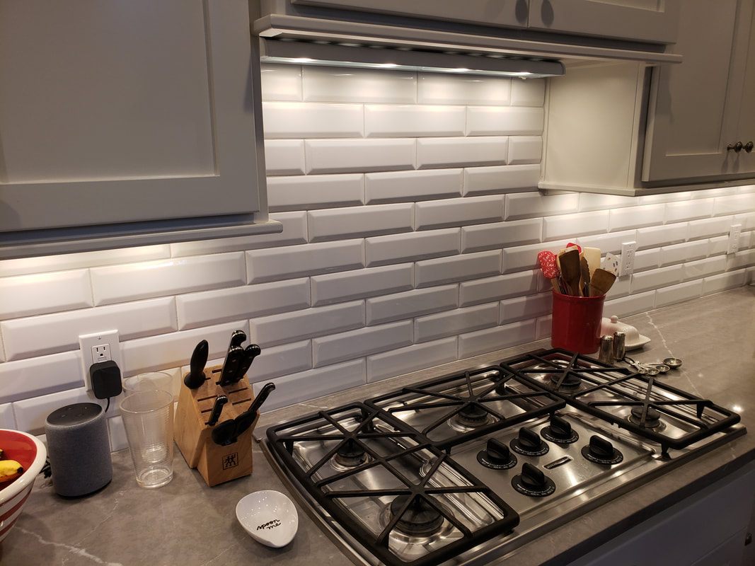 The finished kitchen: white bevelled subway tile backsplash, gray painted cabinets and a light quartz countertop