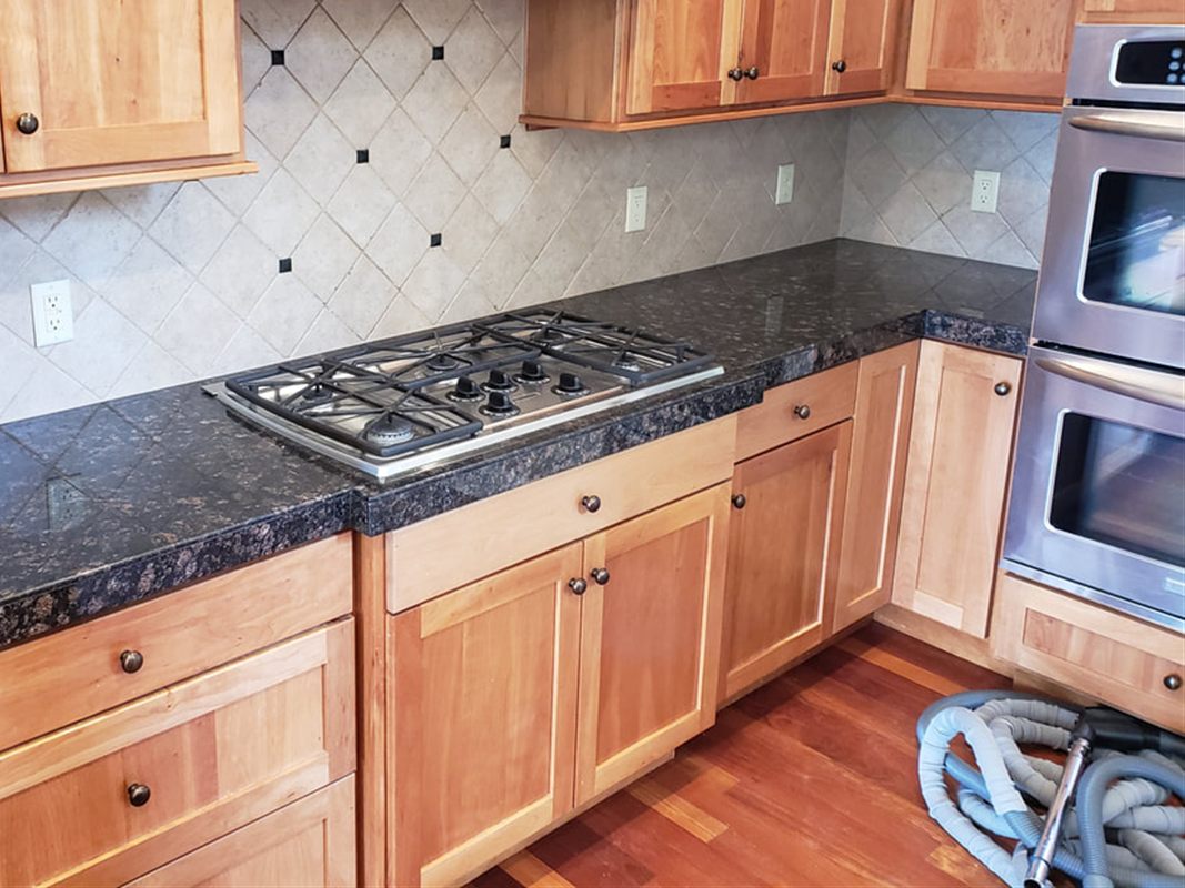The same kitchen before the remodel: oak cabinets, a diamond-set beige tile backsplash and dark granite