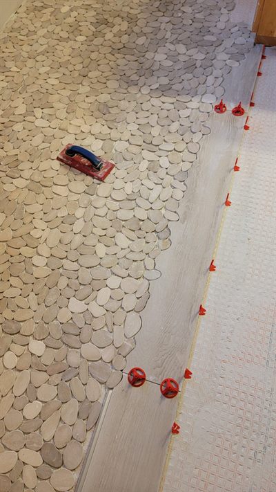 Pebble mosaic floor tile being laid with spacers on a prepared floor