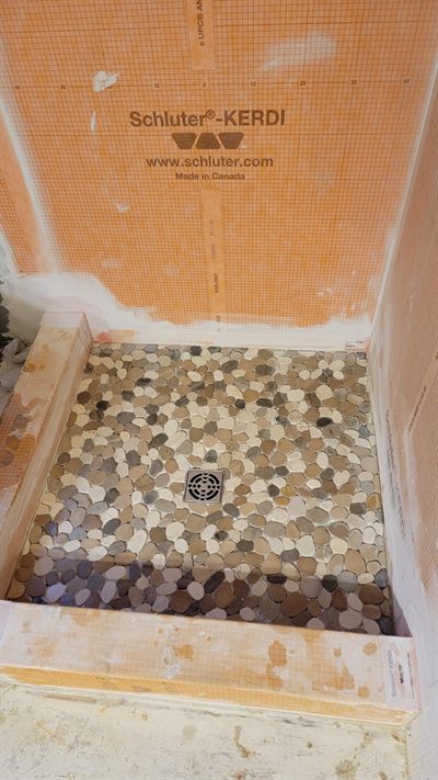 Waterproofed shower pan with pebble tile being set around the drain