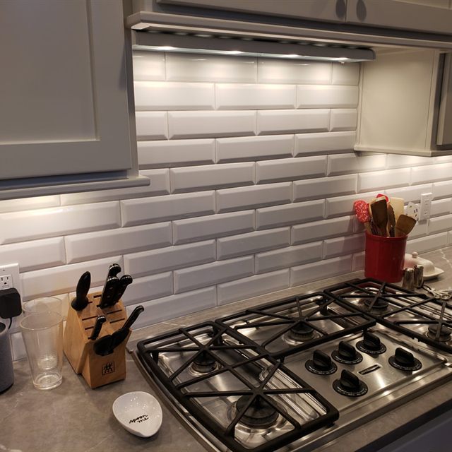White beveled subway tile backsplash with under-cabinet lighting above a stainless gas cooktop