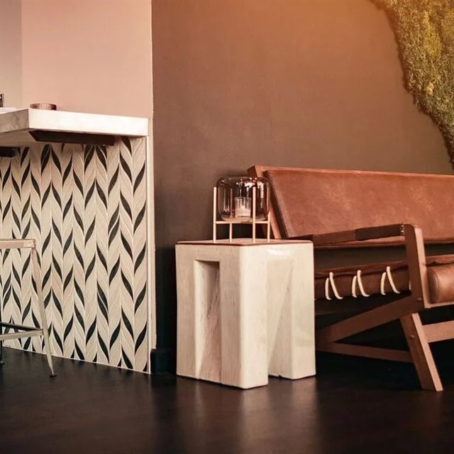 Black, white, and cream chevron mosaic tile cladding on a bar front beside a leather bench.