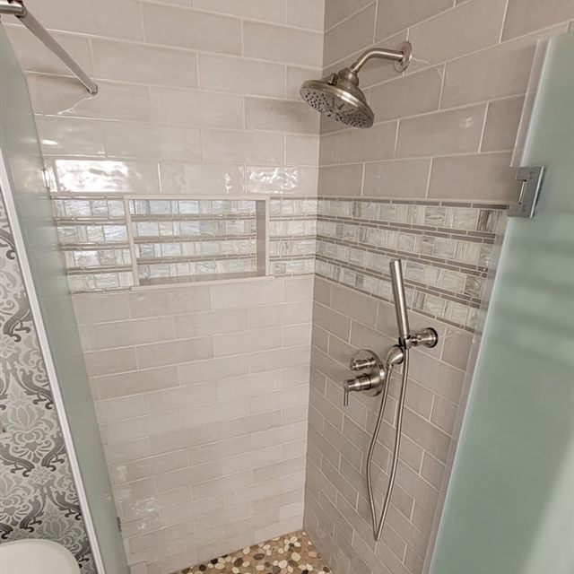 Finished walk-in shower with subway tile walls, mosaic niche, and pebble tile floor