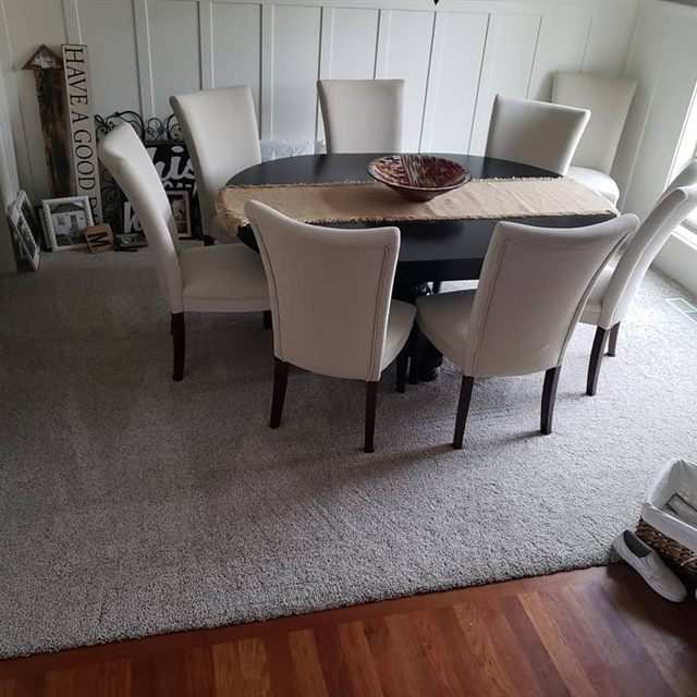 Gray carpet in a dining room with round table and eight chairs, hardwood at the doorway transition