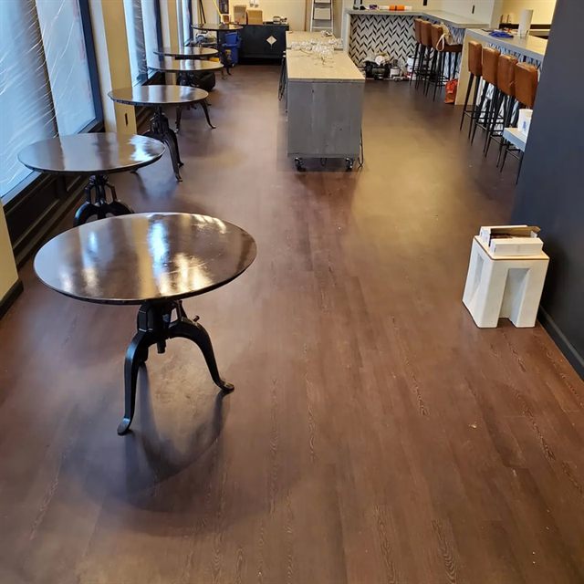 Dark hardwood floor in a commercial dining area with round pedestal tables and a tiled bar in the background.
