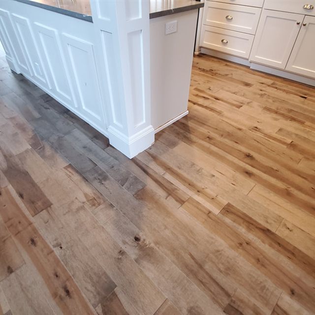 Wood floor beside a white kitchen island, extending toward cabinetry with brass hardware.