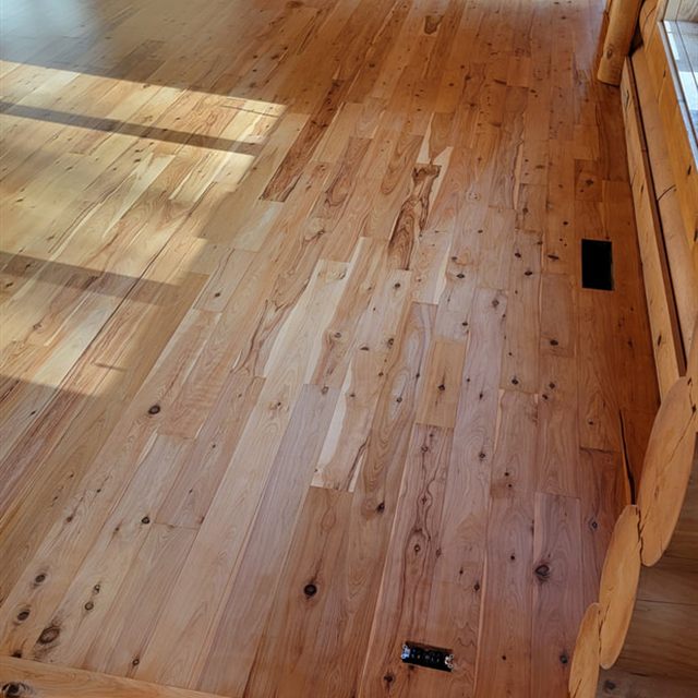 Finished hardwood floor with sunlight streaming across the boards in a log cabin room