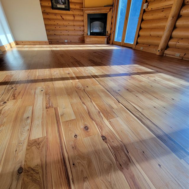 Finished hardwood floor in a log cabin living room with corner fireplace and sunlit floor