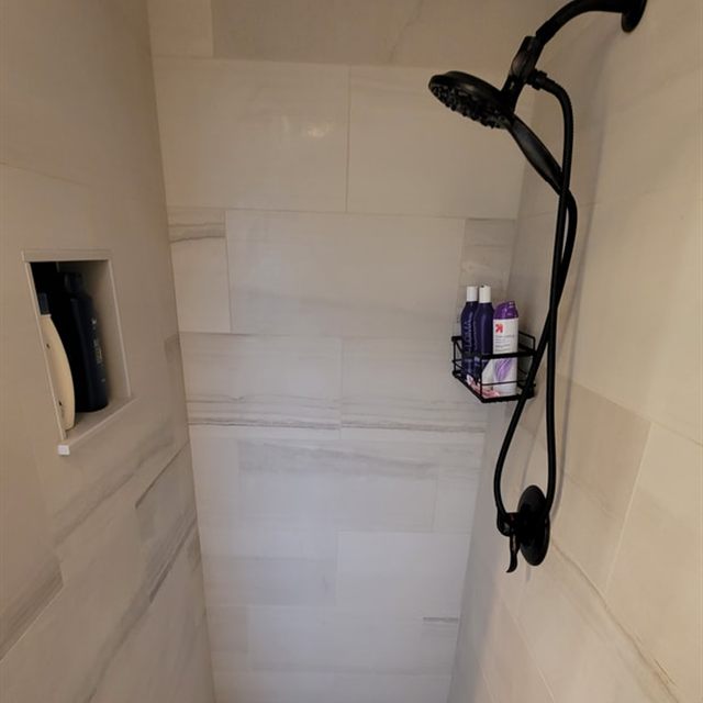 Finished walk-in shower with beige wall tile, black fixtures, and pebble mosaic floor