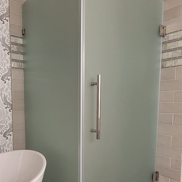 Frosted glass shower door and brushed nickel pull handle beside a freestanding tub