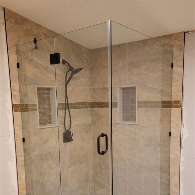 Frameless glass shower with beige tile, bronze fixtures, and pebble mosaic floor
