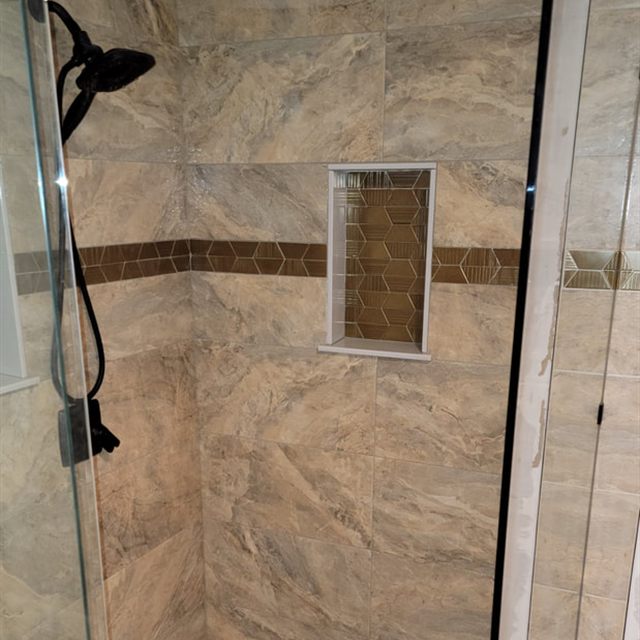 Interior view of finished shower through glass door, showing bronze shower head and pebble floor
