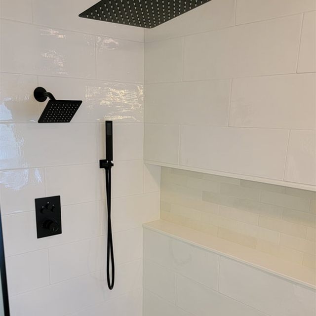 White subway tile shower with black rain shower head, tiled bench, and pebble mosaic floor