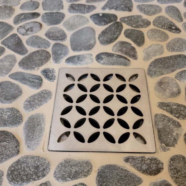 Square stainless steel drain cover in a dark pebble mosaic shower floor