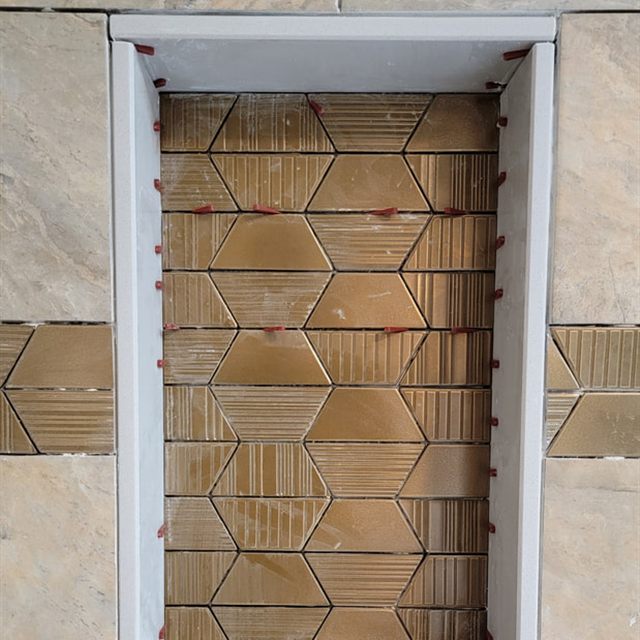 Shower niche with gold hexagonal mosaic tile framed by white trim in stone-look tile wall